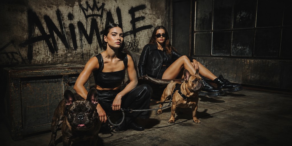 Editorial ANIMALE — dos mujeres y bulldogs franceses frente a un muro con graffiti industrial
